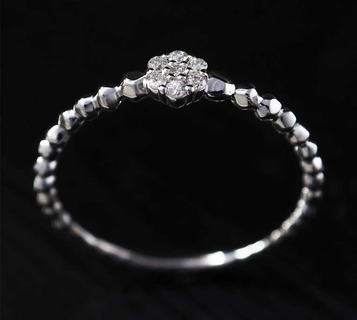 黒い背景に、中央に花のようなダイヤモンドが配置された華奢なシルバーまたはプラチナの指輪