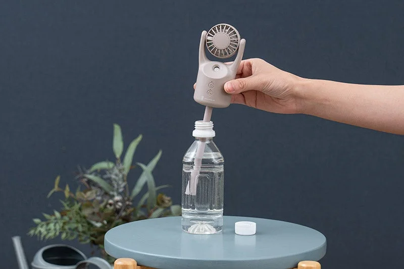 手がペットボトルに差し込まれた携帯型の扇風機兼ミストスプレーのようなデバイスを持っている様子。夏の暑さ対策や乾燥対策に役立つガジェットです。
