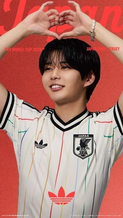 白いアディダスの日本代表アウェイユニフォームを着た若い男性が、両手でハートマークを作り笑顔を見せている