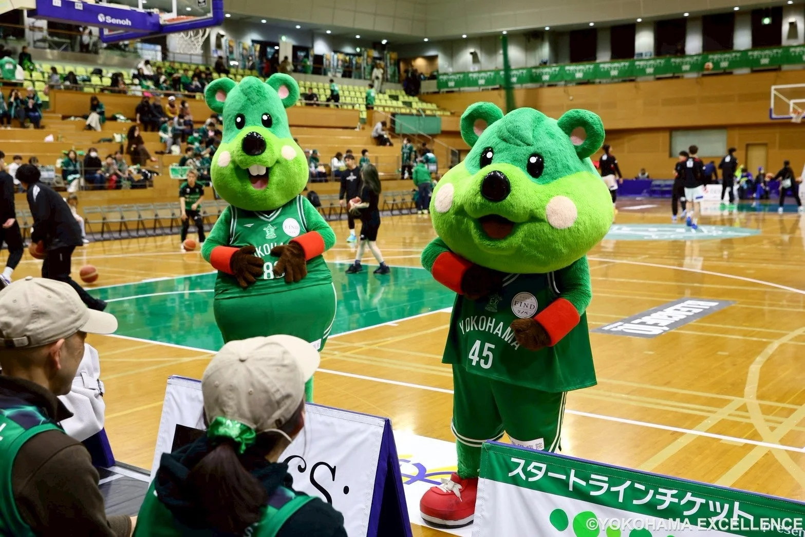 バスケットボールの試合会場で、緑色のマスコットキャラクターが2体立っている