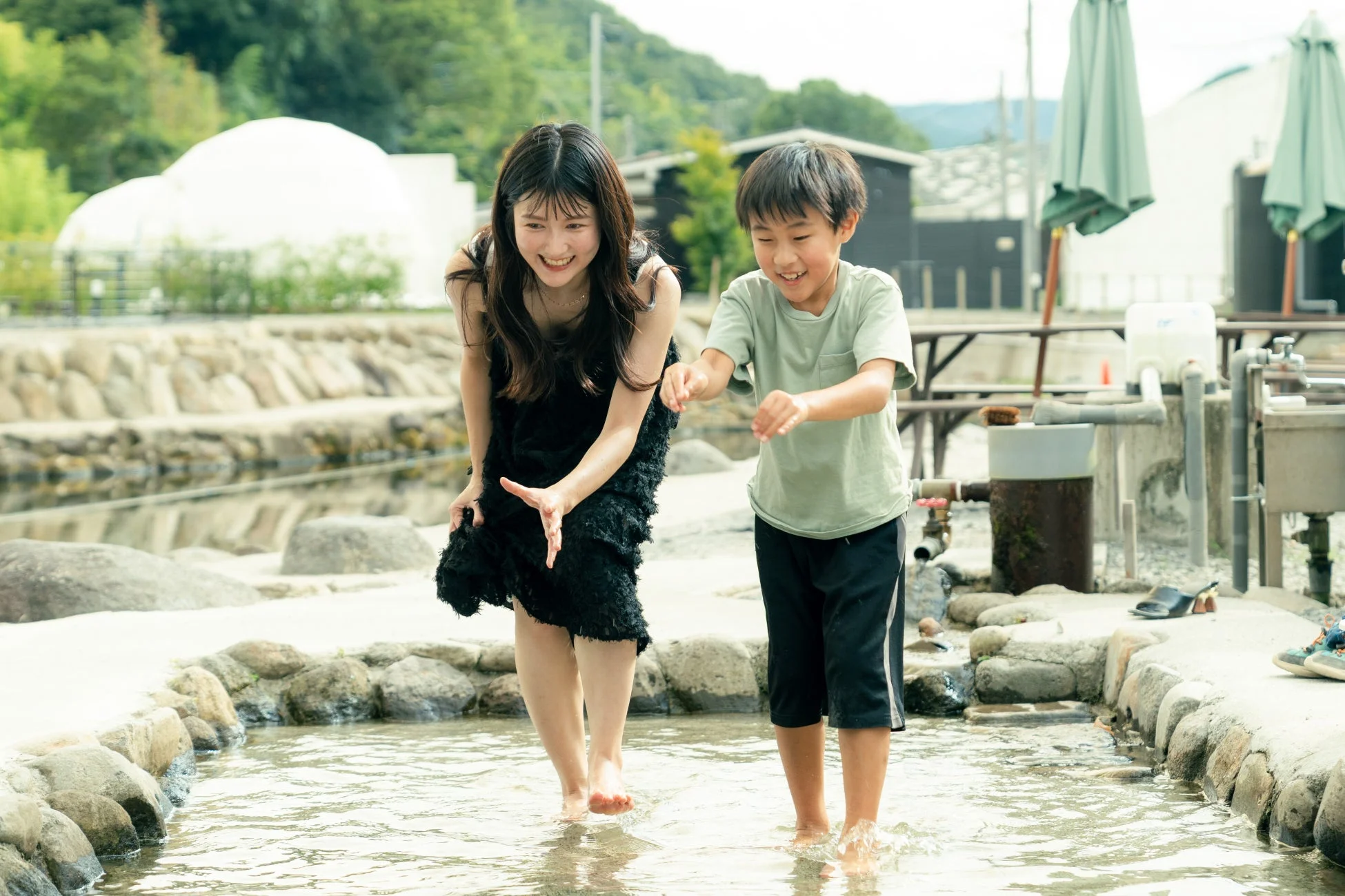 屋外で笑顔の女性と男の子が裸足で水遊びを楽しんでいる