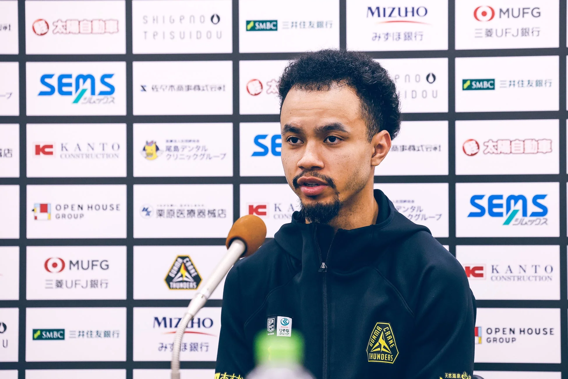 黒いパーカーを着た男性がマイクの前で話している