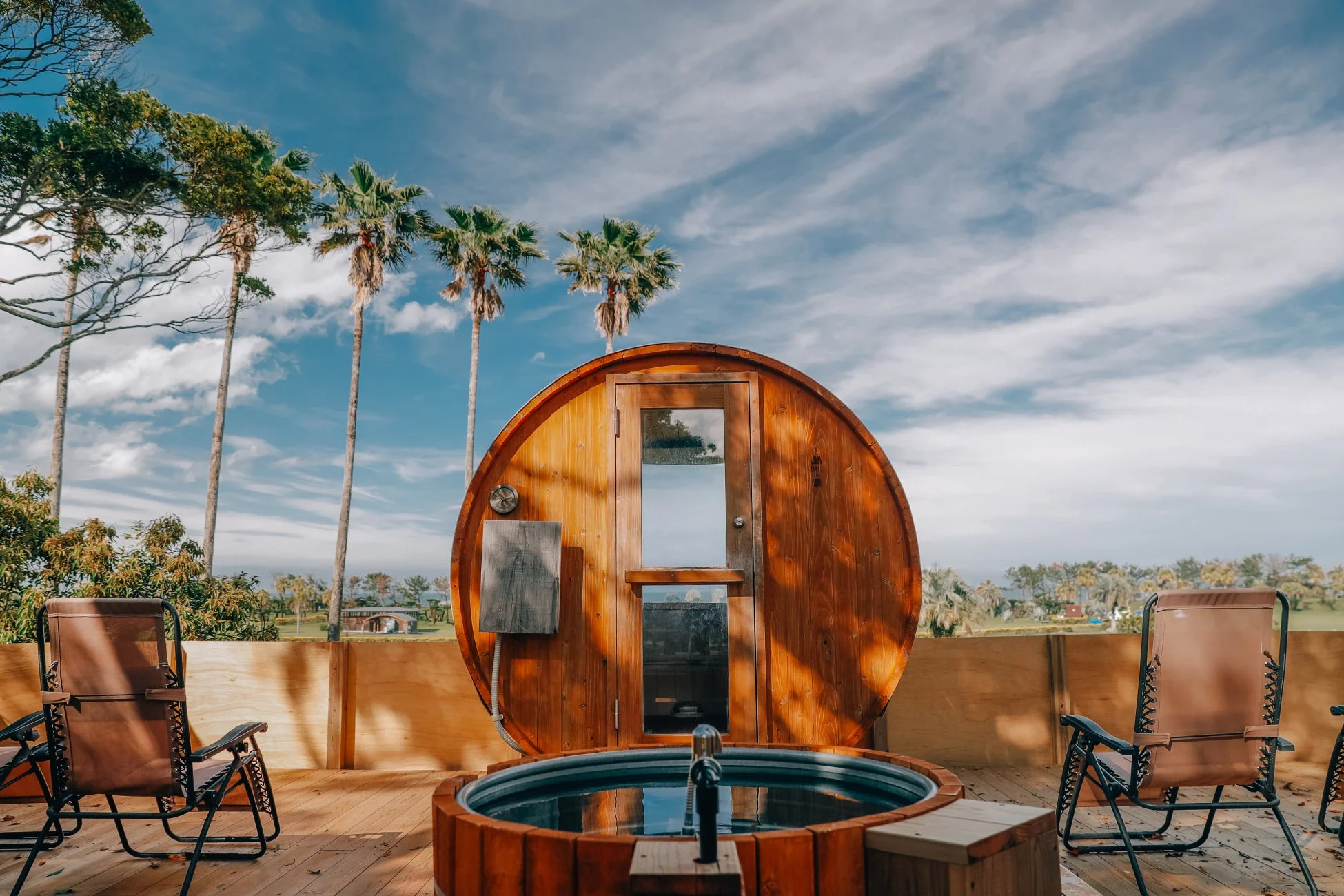 青空の下、木製デッキにバレルサウナと水風呂が設置されたリゾート感あふれるアウトドア空間。