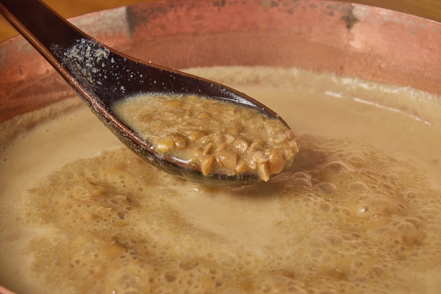 銅製の鍋で煮込まれている茶色いスープをスプーンですくっているクローズアップ写真