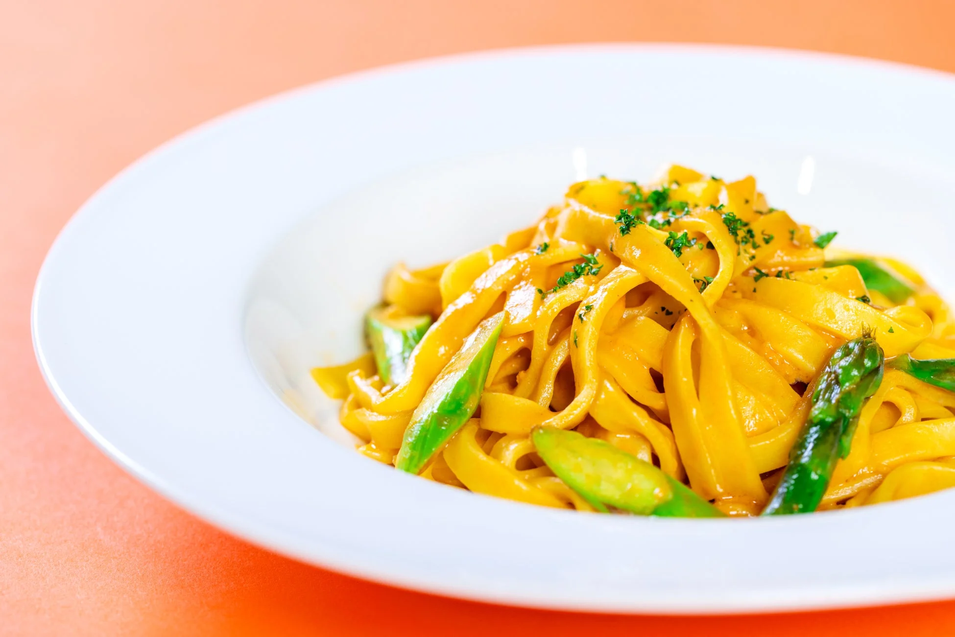 白い皿に盛られた、オレンジ色の背景に映えるクリームソースのフェットチーネ