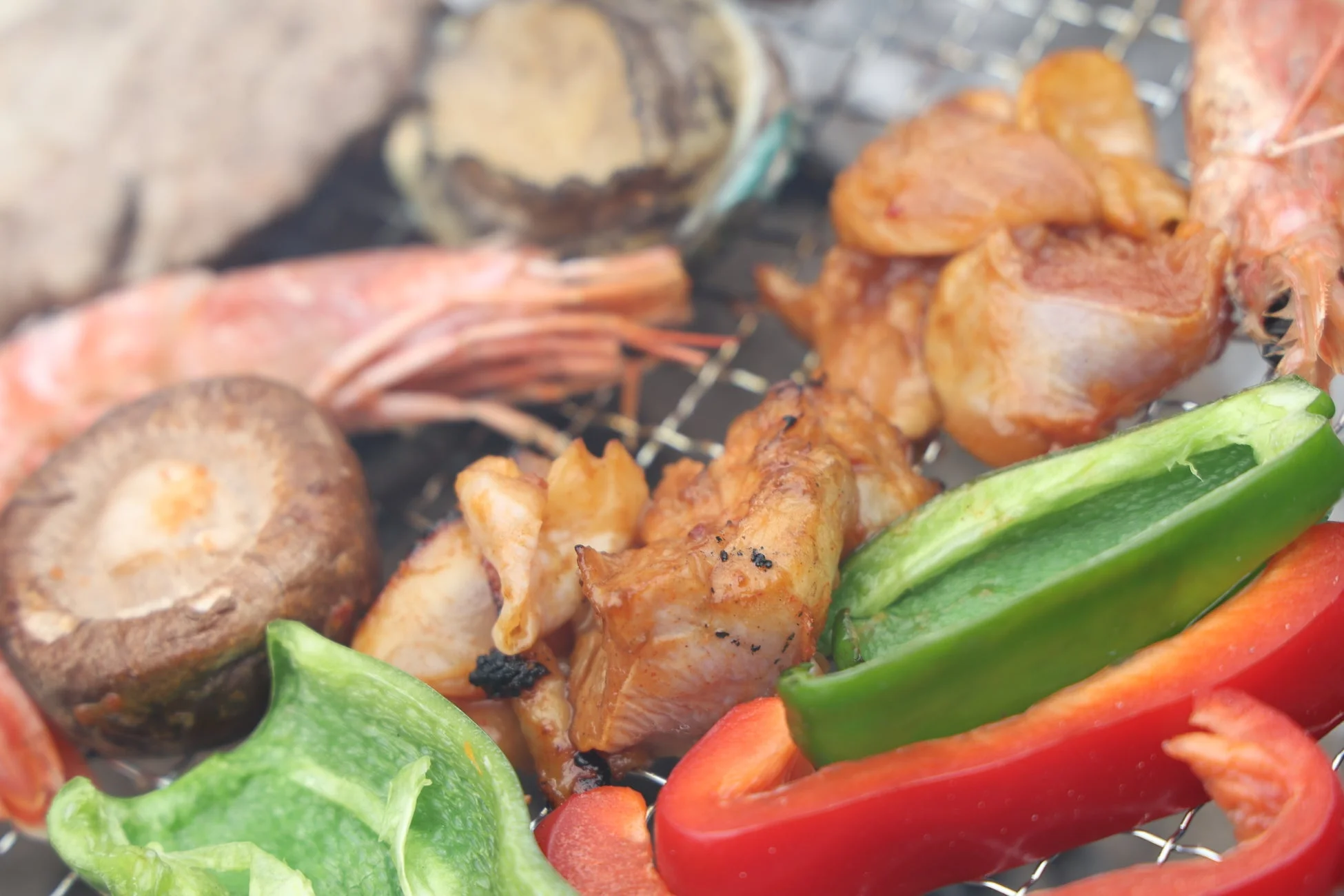 網の上でエビ、しいたけ、パプリカなどの海鮮や野菜が焼かれているバーベキューの様子