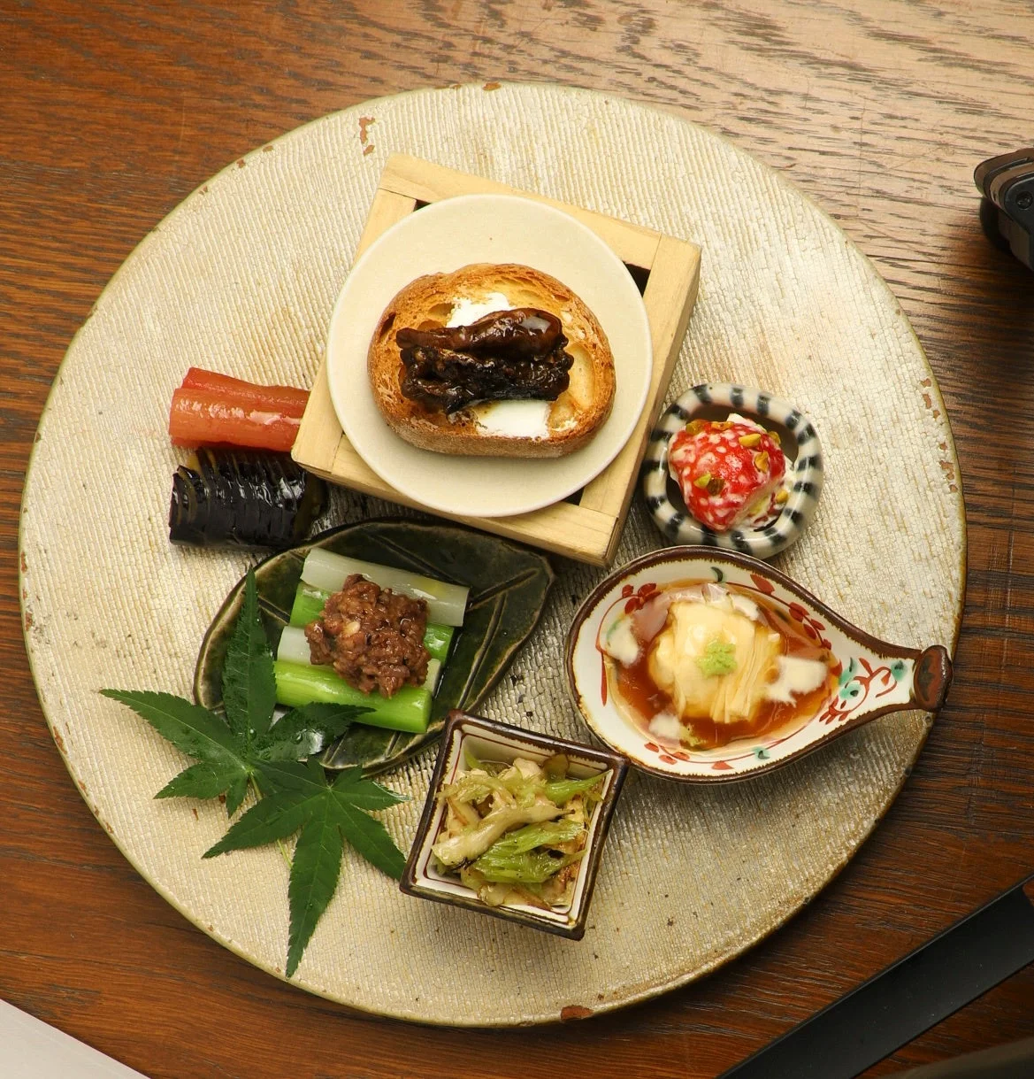 木製のテーブルに置かれた大きな皿に、彩り豊かな和食の前菜が美しく盛り付けられています。