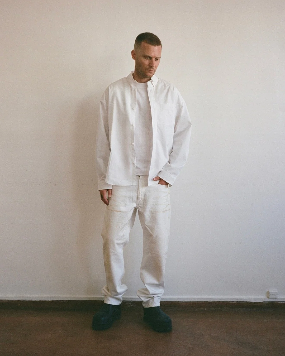 白いスタンドカラーシャツと白いパンツを着用した男性