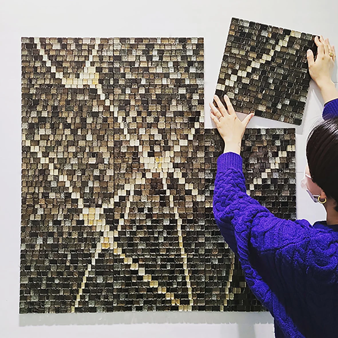 木片を組み合わせたモザイクアートを壁に設置する様子