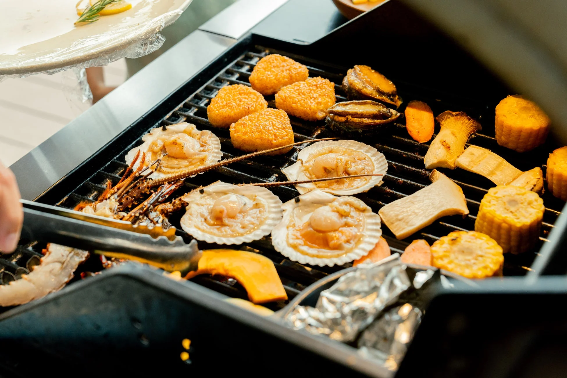 バーベキューグリルでホタテ、アワビ、焼きおにぎり、トウモロコシ、キノコなどの多様な食材が焼かれている