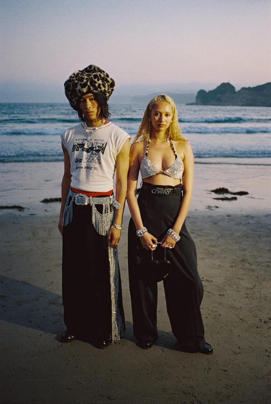 夕暮れのビーチでポーズをとる男女のモデル。ヒョウ柄の帽子やスパンコールのビキニトップなど、個性的なファッションスタイルを披露しています。