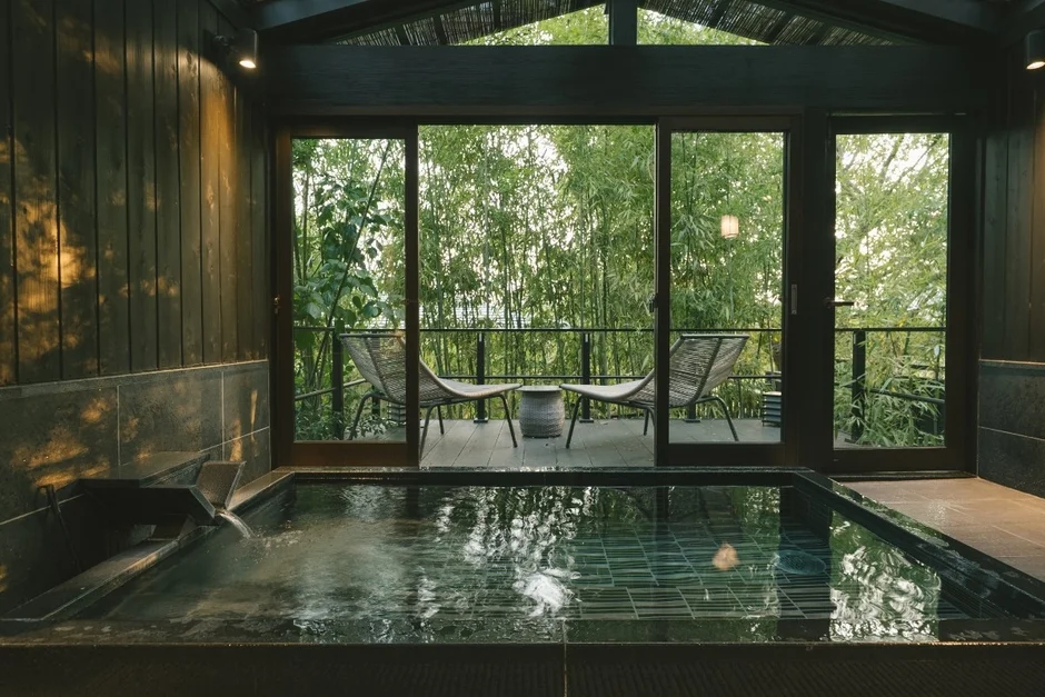 竹林に面したプライベートな露天風呂とテラスがある、和モダンな宿泊施設の風景。屋外の椅子からは緑豊かな景色が広がり、贅沢な癒しの空間を提供している。