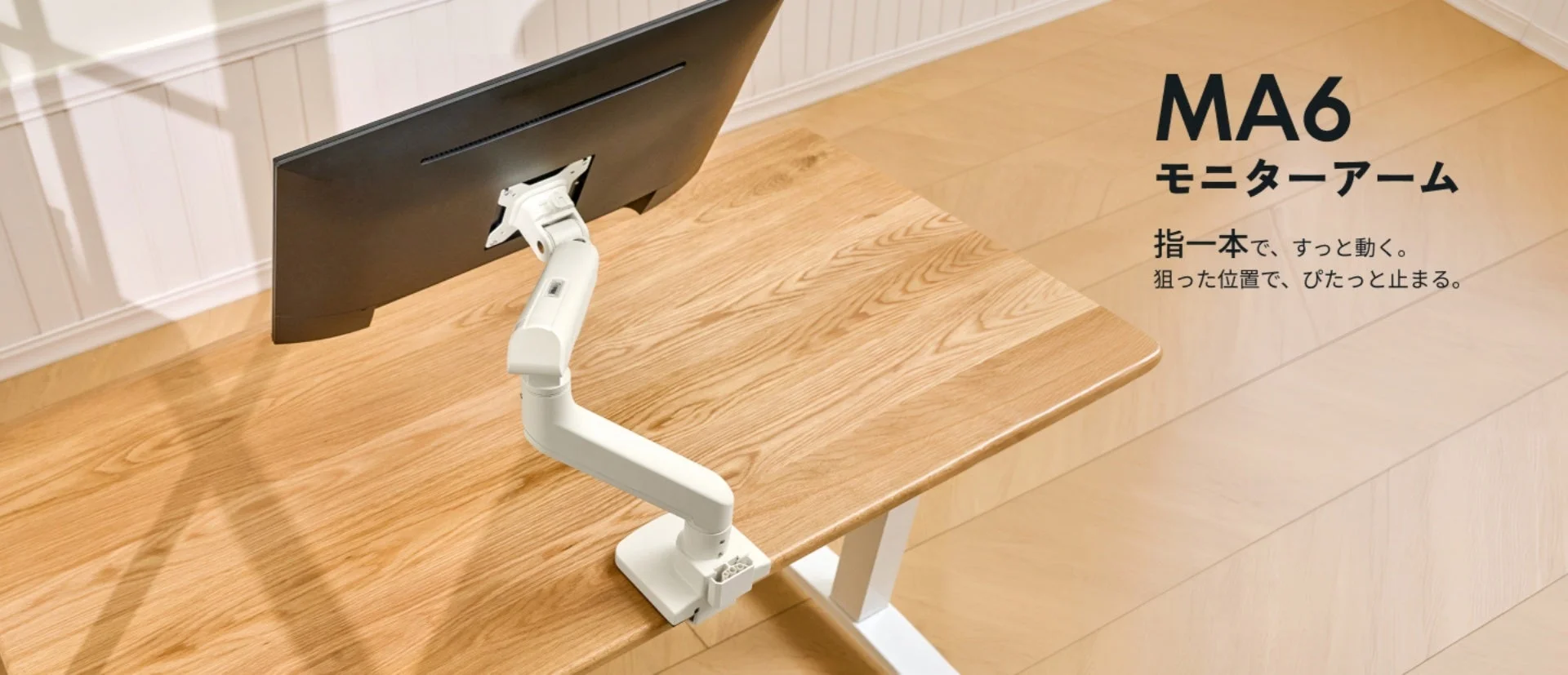 木目調のデスクに設置された白色のMA6モニターアームが、モニターを支えている様子を捉えた画像です。指一本でスムーズに動き、狙った位置で固定できるという製品の特徴が示されています。