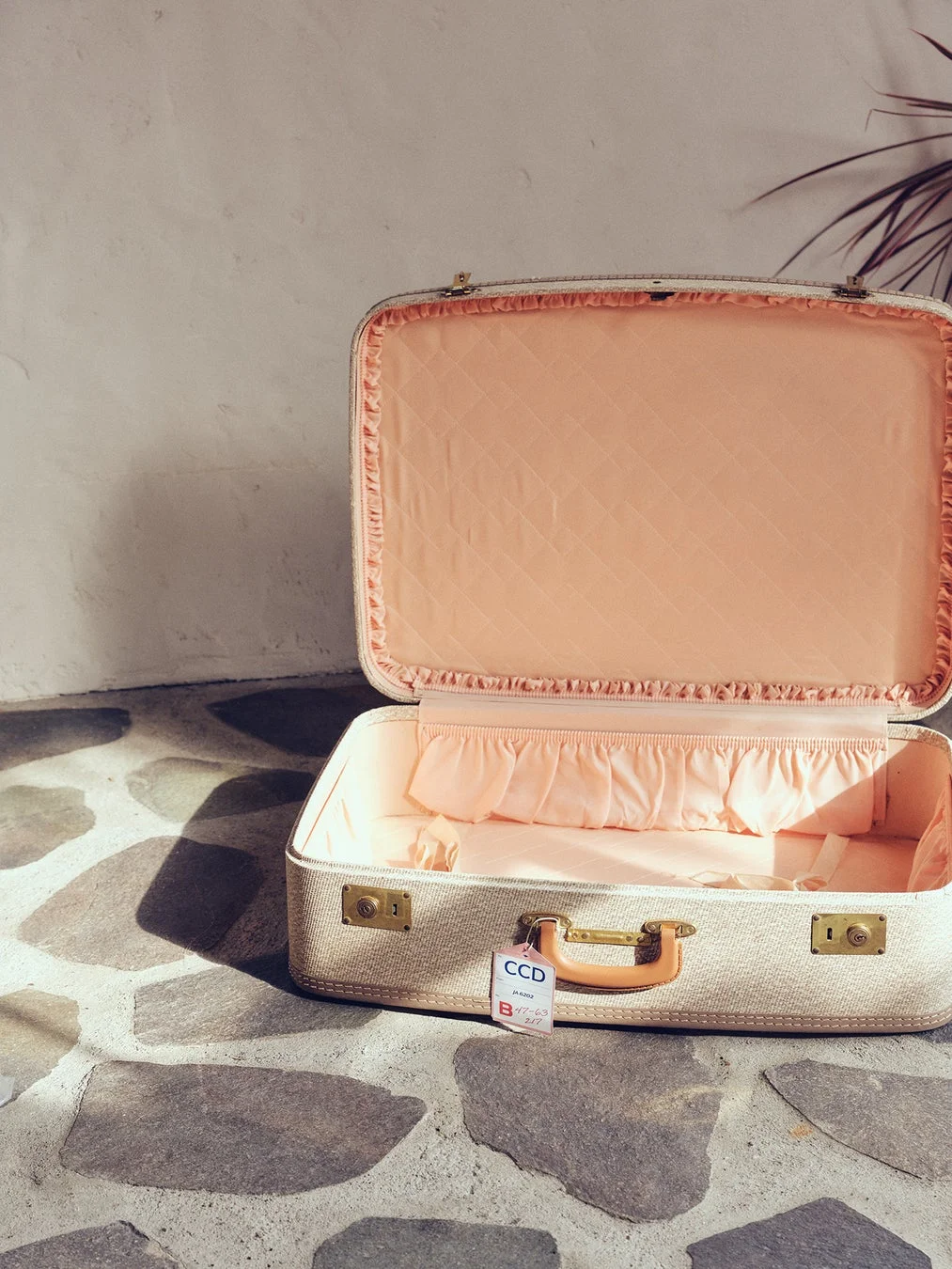 開いた状態のヴィンテージ風スーツケースが石畳の上に置かれている画像です。