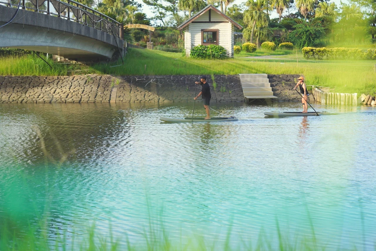 自然豊かな水辺で、2人の人物がパドルボードを楽しんでいる様子。