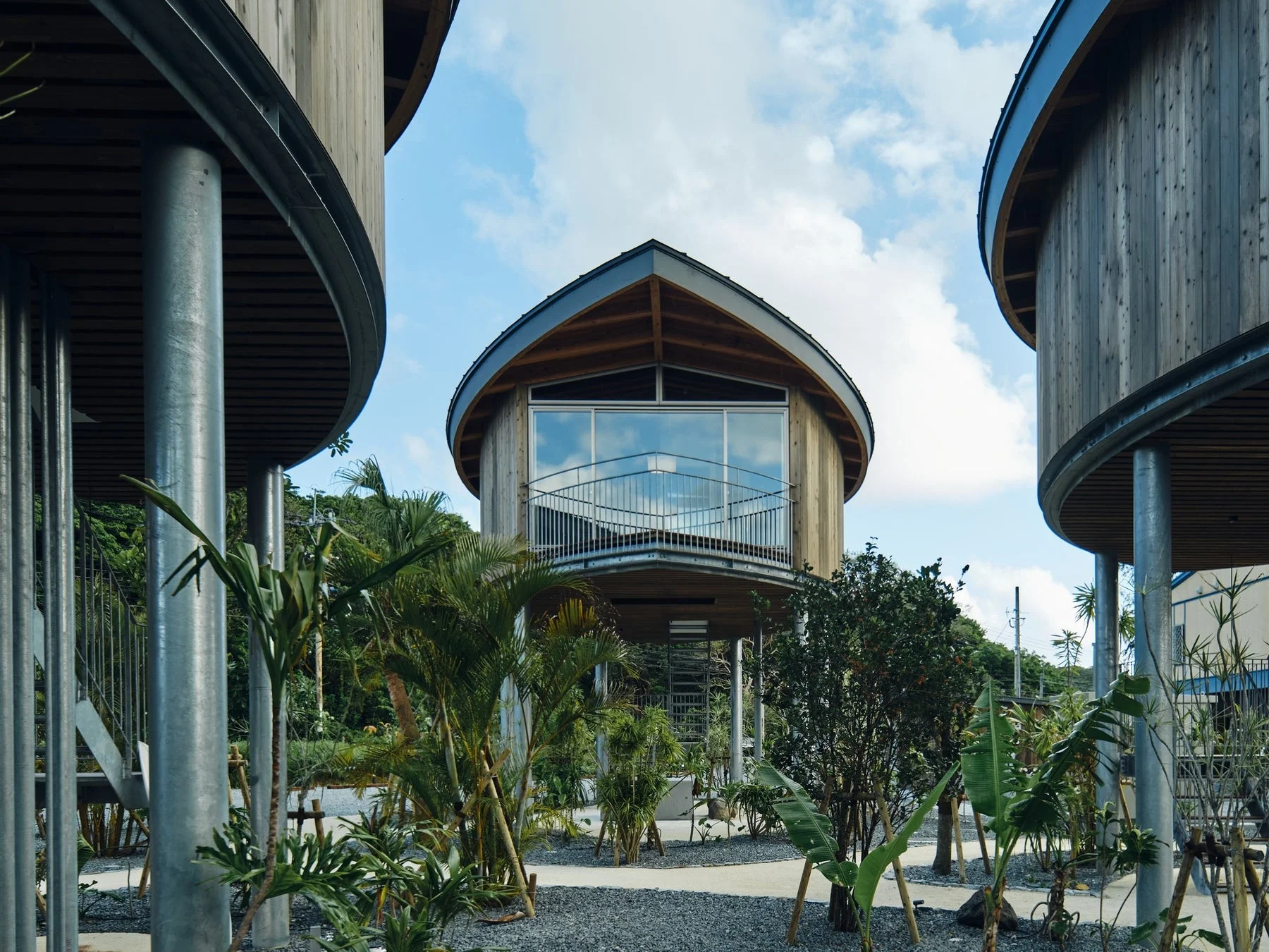 青空の下、熱帯植物に囲まれた高床式のモダンな円形木造建築群