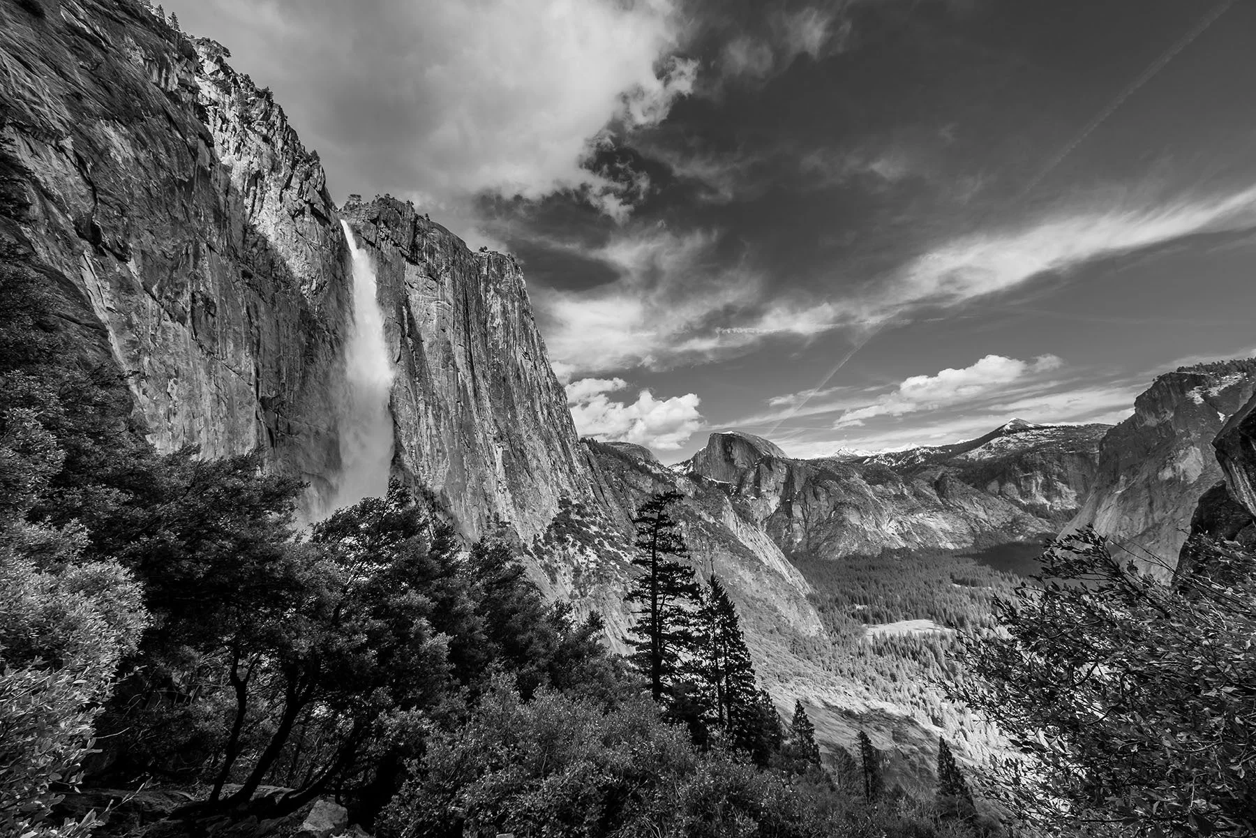 ヨセミテ国立公園の壮大なモノクロ風景で、巨大な崖から流れ落ちるヨセミテ滝と、遠くに見えるハーフドームが特徴です。