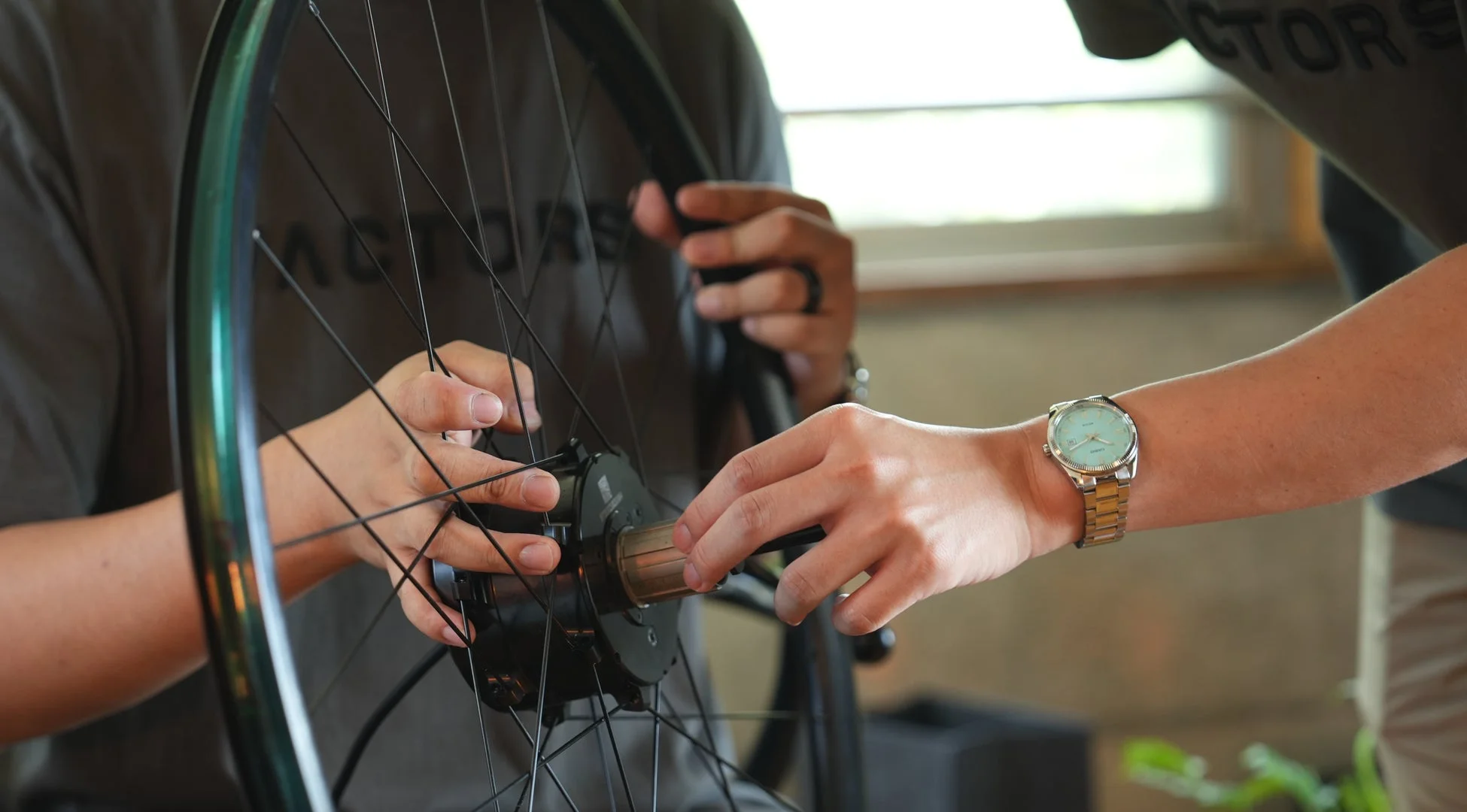 二人の人物が協力して自転車のホイールのハブ部分を調整している様子