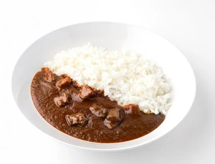白い皿に盛られたご飯と、具材の肉が見える濃厚なブラウンのルーがかかったカレーライスです。