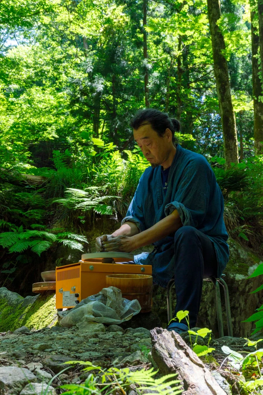 豊かな緑に囲まれた森の中で、一人の日本人男性が電動ろくろを使って陶芸に没頭している