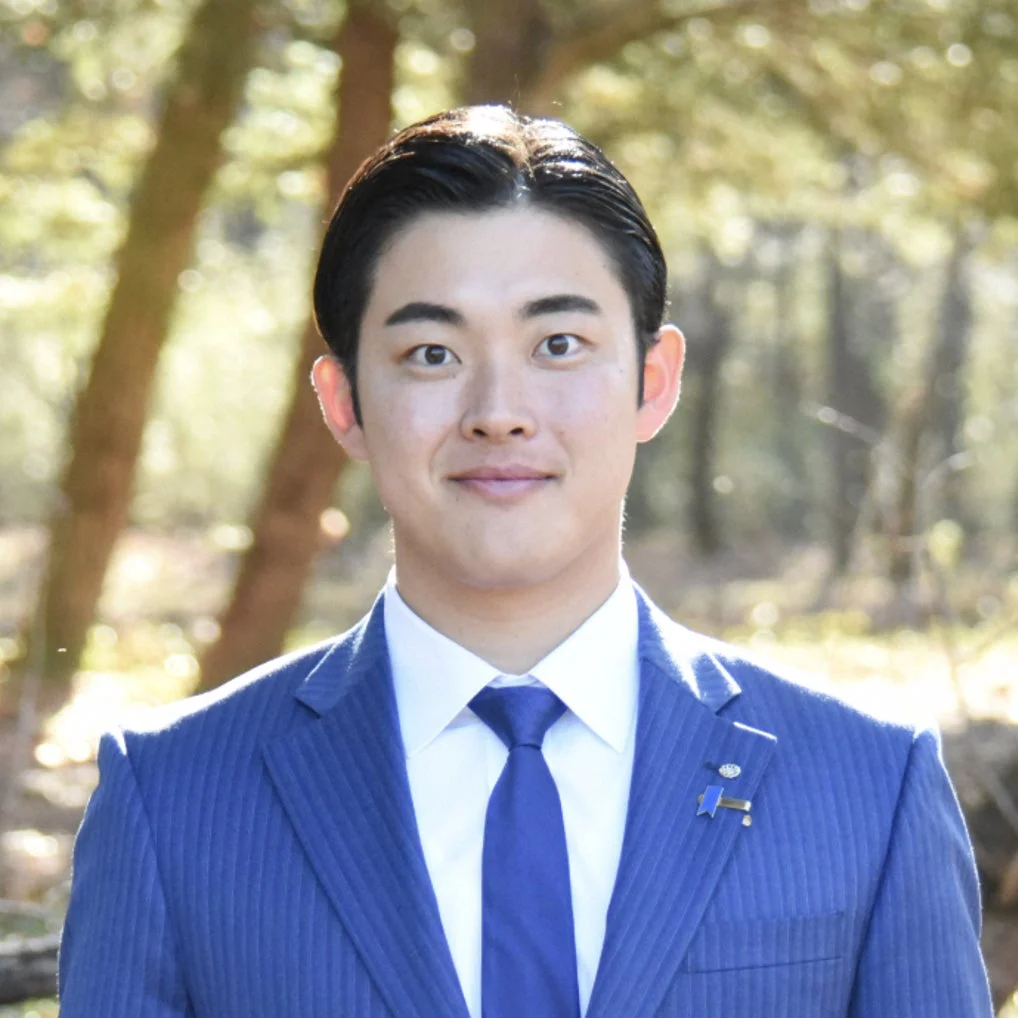 青いスーツの男性が屋外で笑顔でカメラを見ている