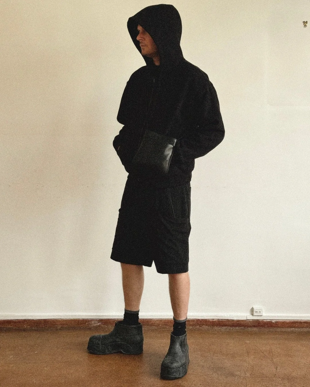 全身黒のパーカー、ショートパンツ、厚底ブーツを着用した男性
