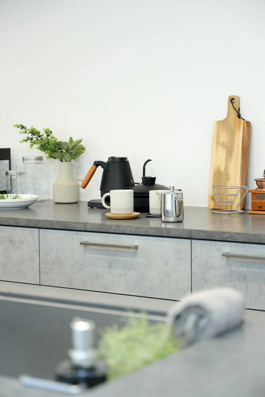 モダンなキッチンカウンターに、コーヒー器具や観葉植物、カッティングボードなどが整然と並べられています