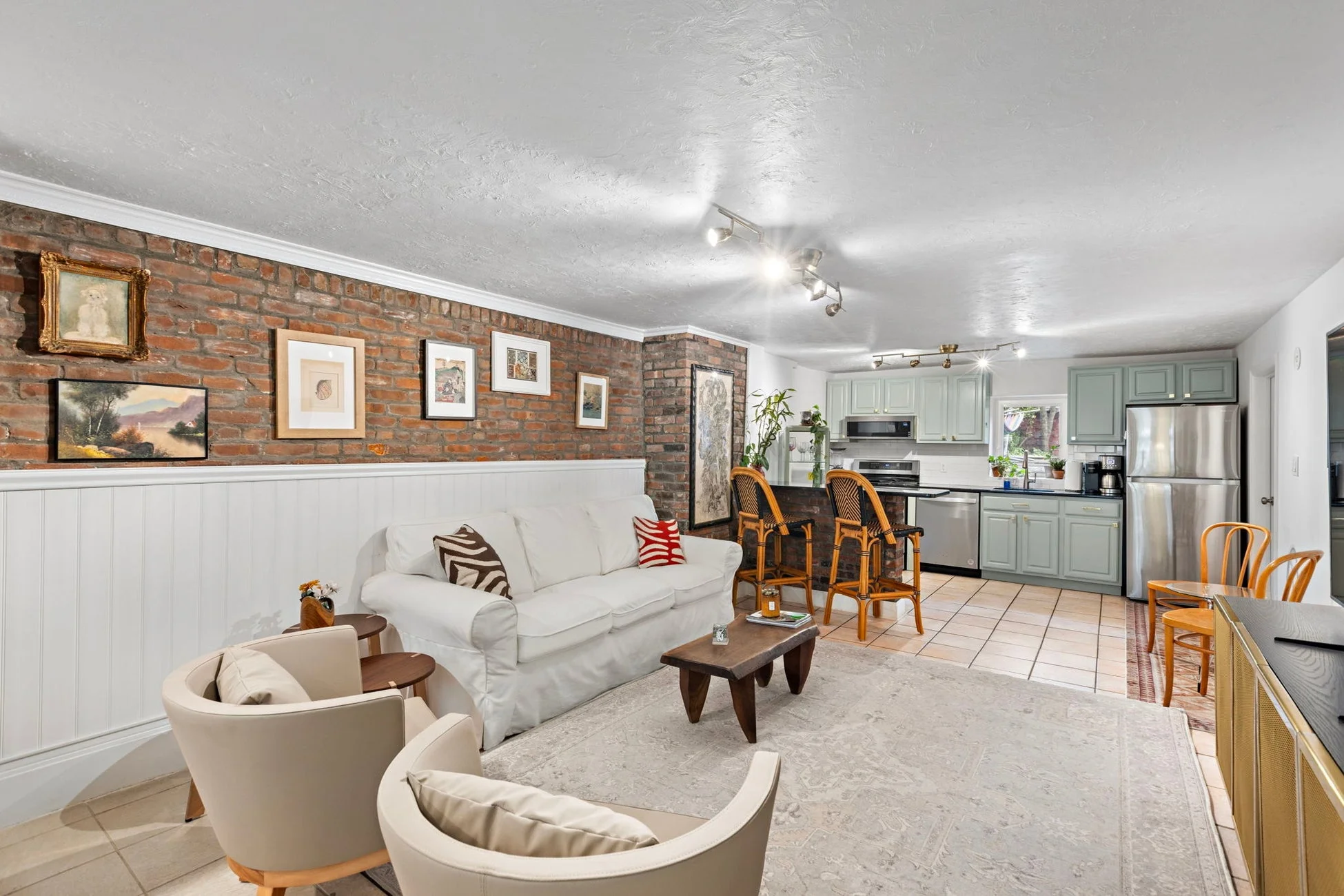 レンガの壁と白い腰壁が特徴的な、リビングとキッチンが一体となったオープンコンセプトの空間