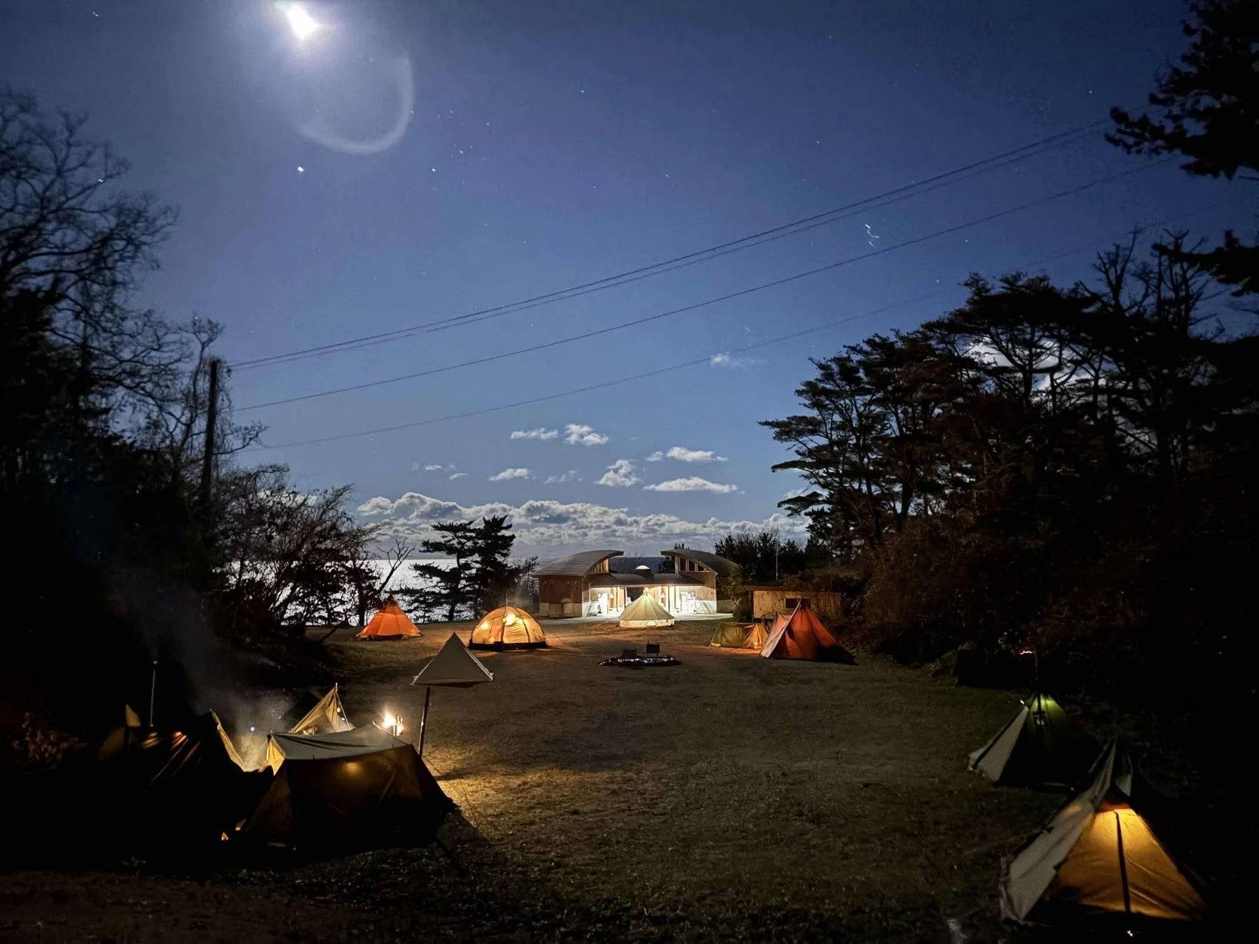 月明かりの下、複数のテントが並ぶキャンプ場の夜景