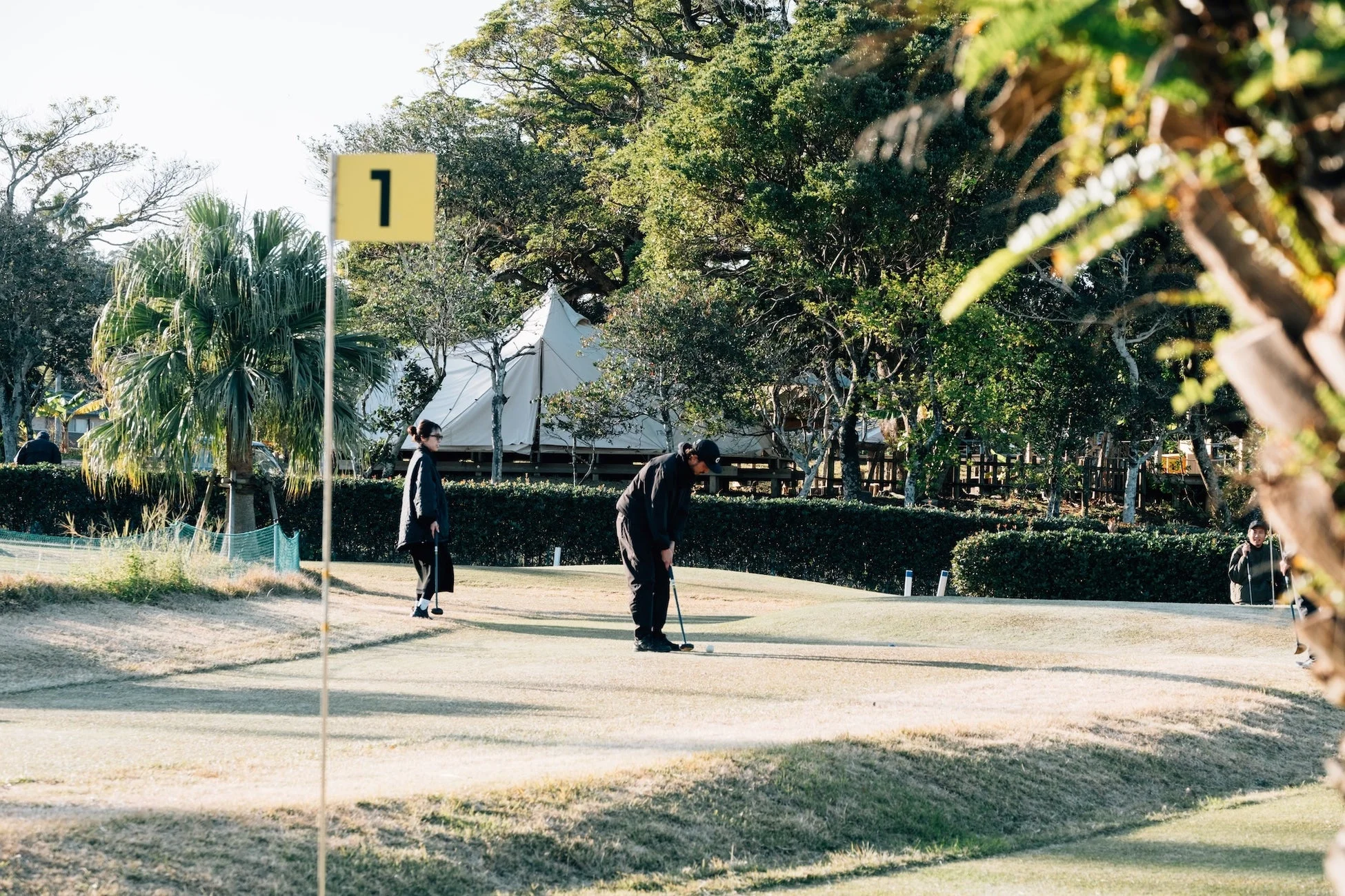 ゴルフ場でパッティングをする男性とそれを見守る女性の様子が捉えられています。