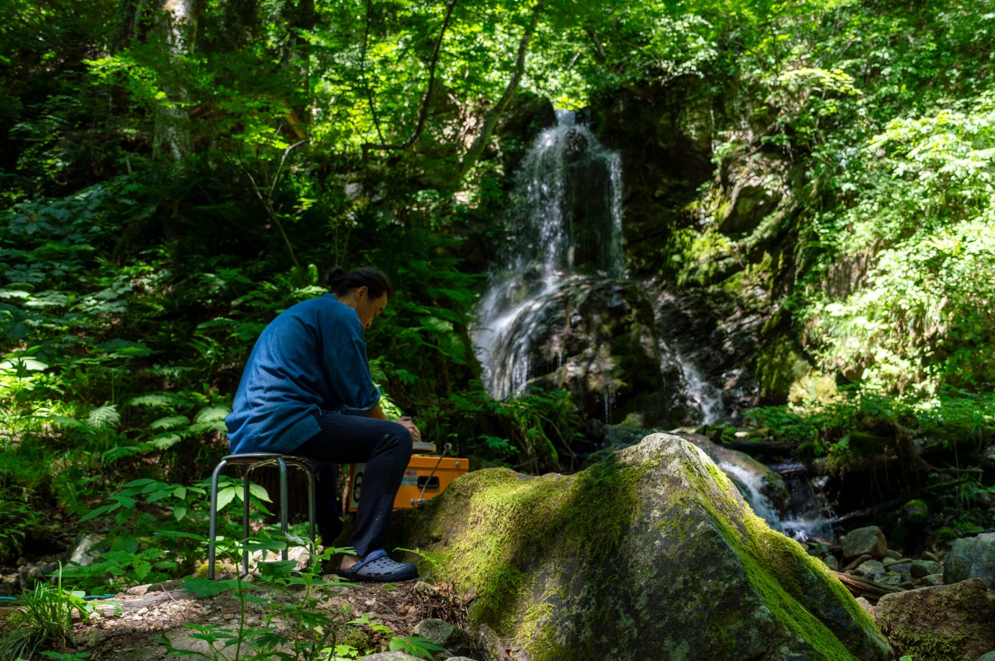 緑豊かな森の中で、女性が滝を背景に写生をしている