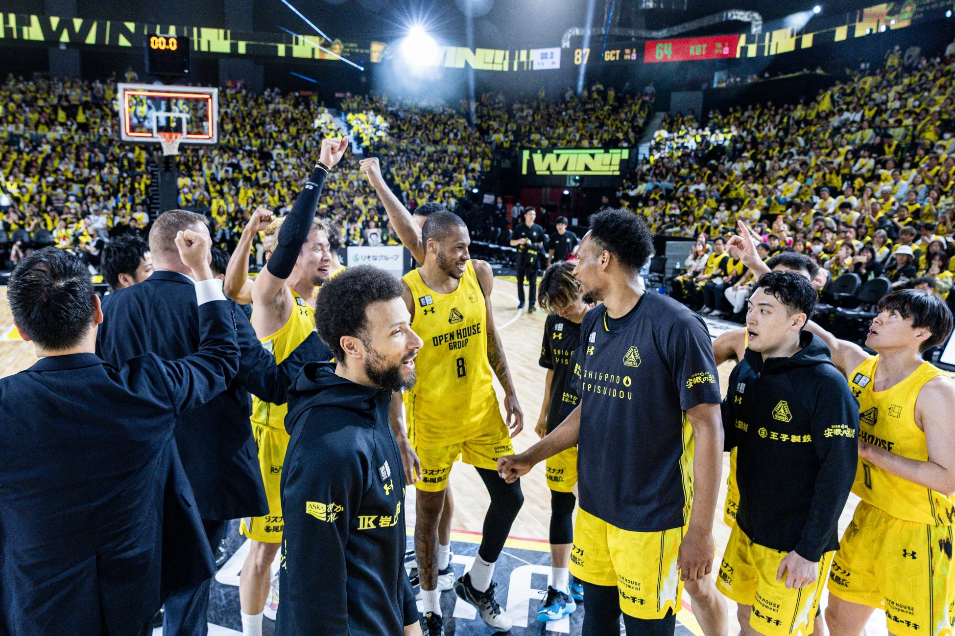 バスケットボールの試合会場で、多くの観客が見守る中、選手やコーチたちが勝利を祝っている瞬間