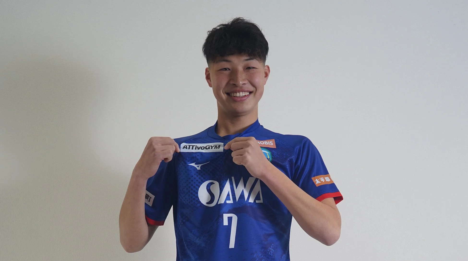 青いスポーツユニフォームを着た若い男性が、笑顔でカメラを見つめています