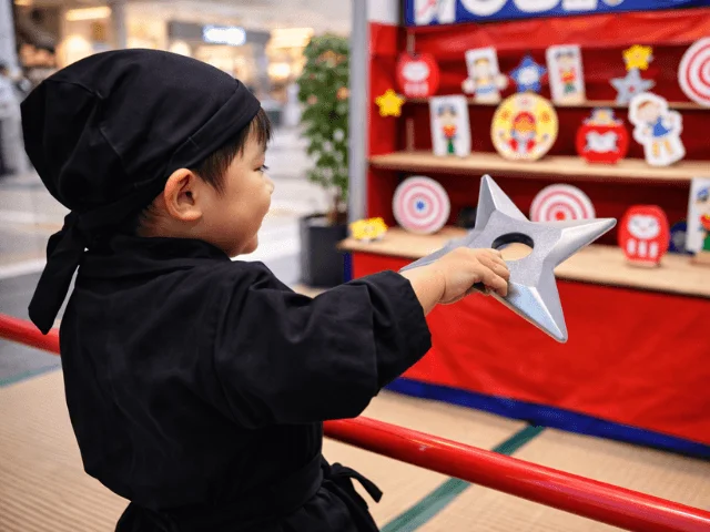 忍者の衣装を着た子供が手裏剣を手に、的当てゲームを楽しんでいる様子