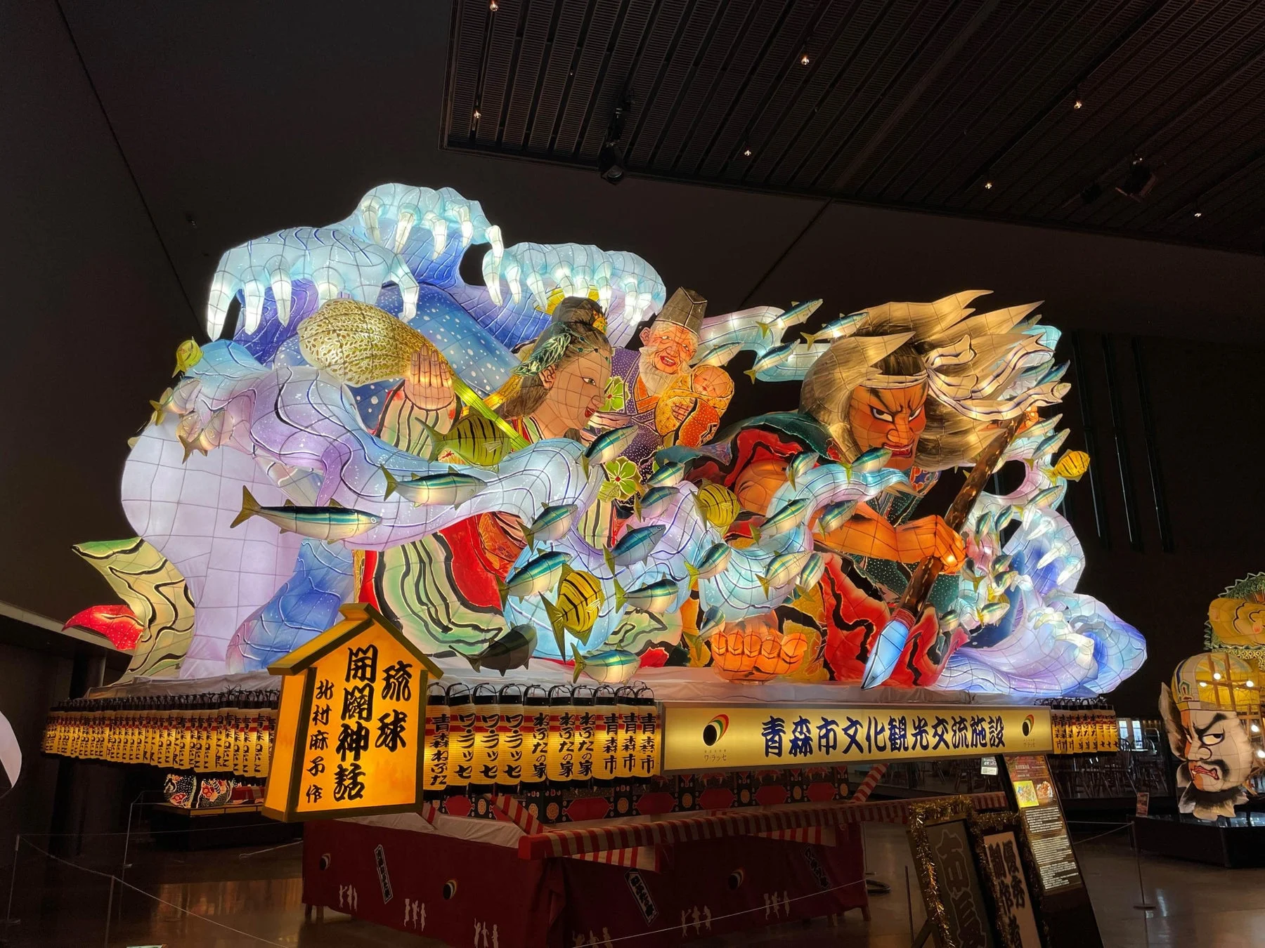 暗い屋内に展示された、鮮やかに光る巨大なねぶたの山車です。