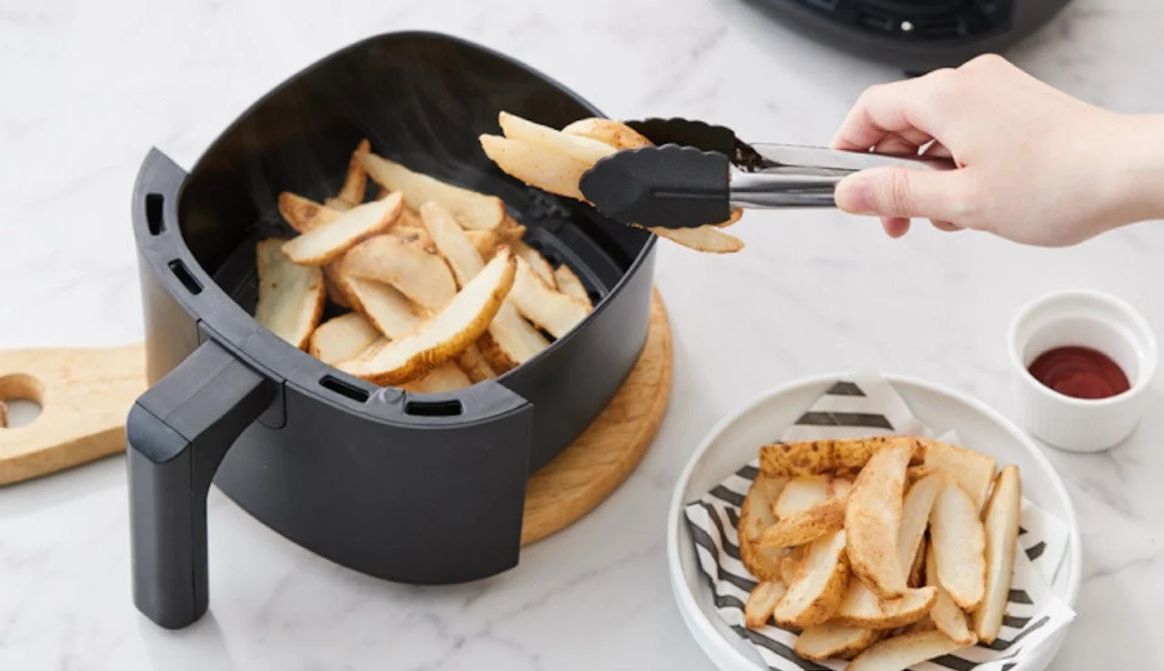 エアフライヤーで調理されたポテトウェッジをトングで皿に移す様子