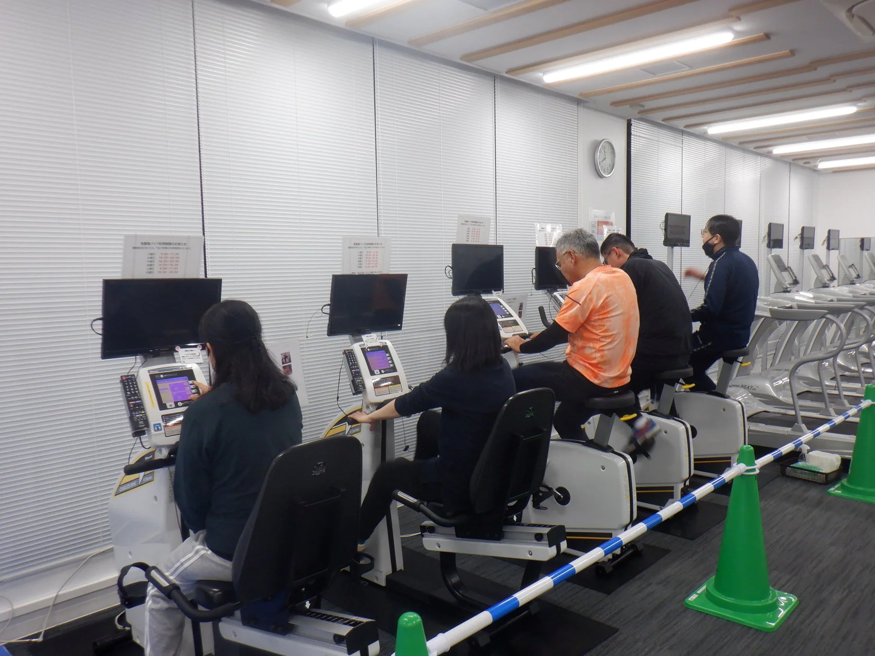 フィットネス施設内でエアロバイク型運動器具を使用する人々