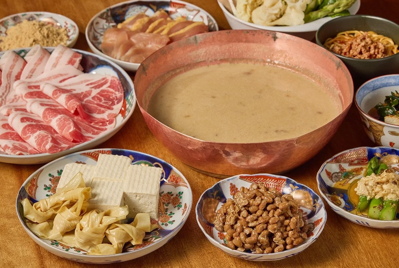 豚肉、鶏肉、豆腐、湯葉、納豆など様々な具材が銅鍋の周りに並べられた日本の鍋料理の準備風景