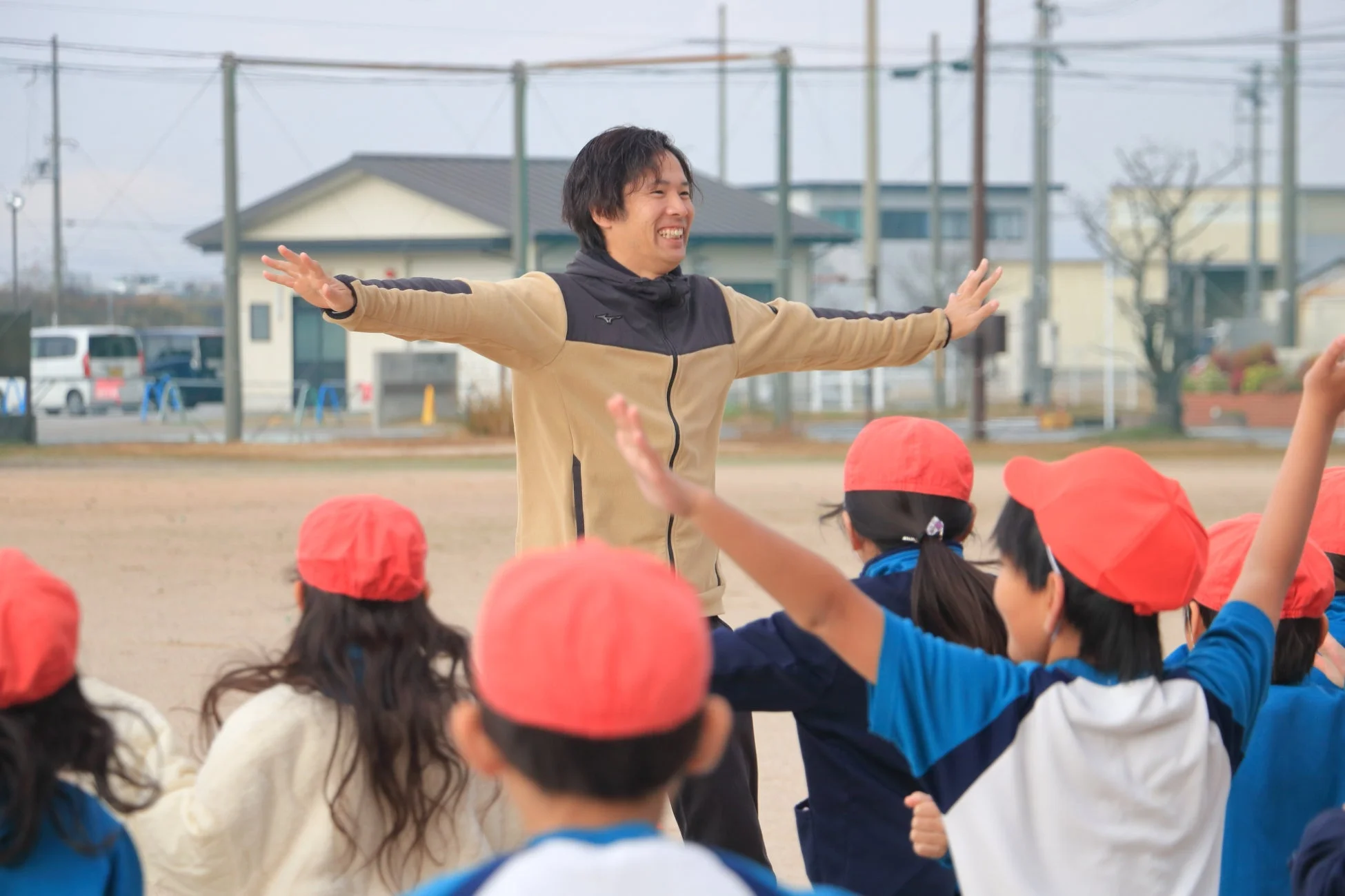 屋外の運動場で体操を教える男性指導者と子供たち