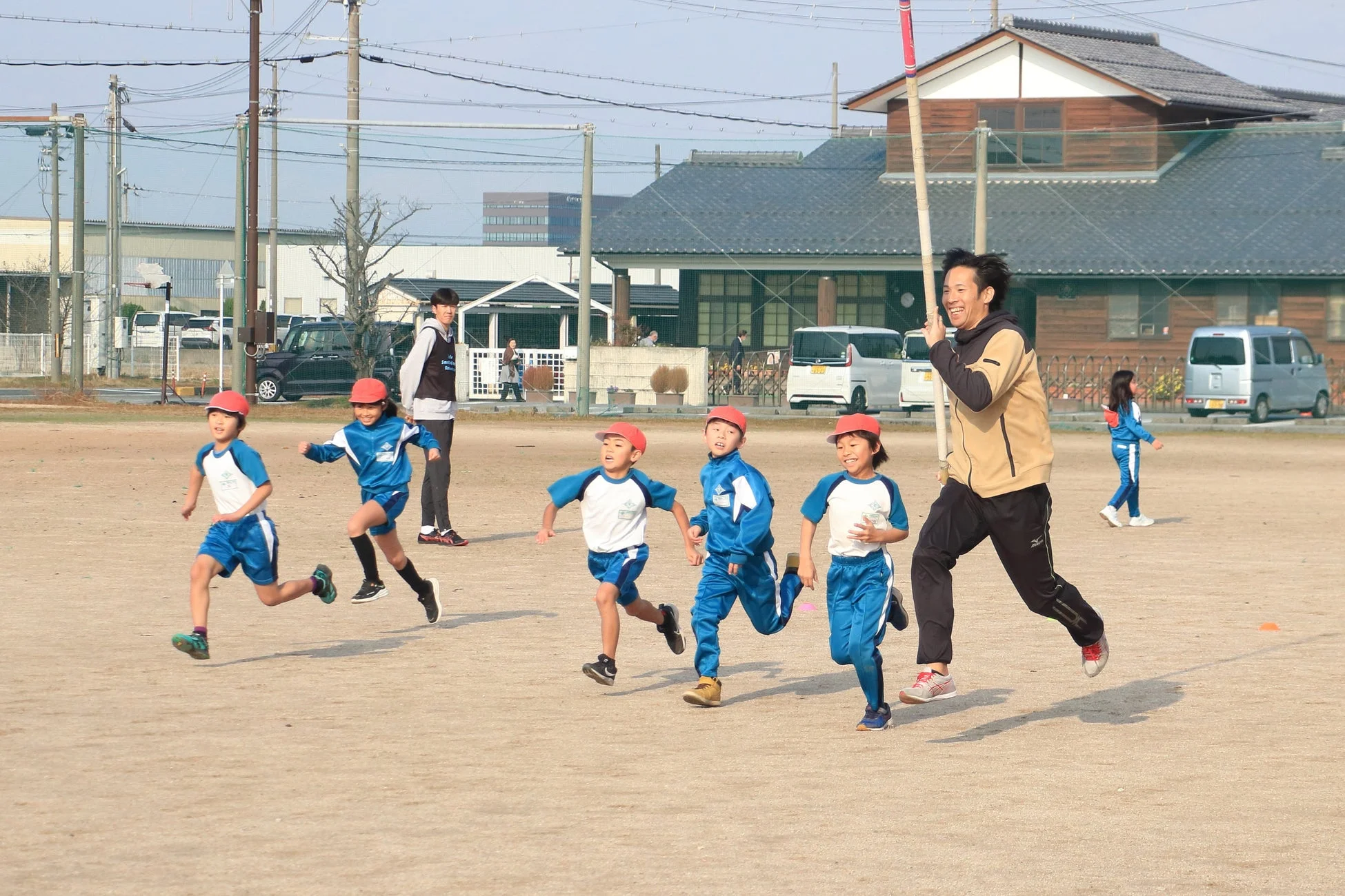 屋外のグラウンドで走る子供たちと男性指導者