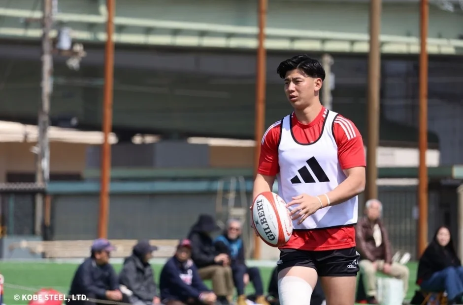 ラグビー選手が赤いシャツと白いビブスを着用し、ラグビーボールを持って練習している