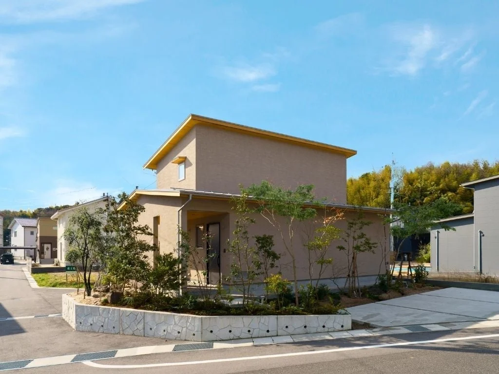 晴れた青空の下、ベージュの外壁と黄色い屋根が特徴的なモダンな一軒家