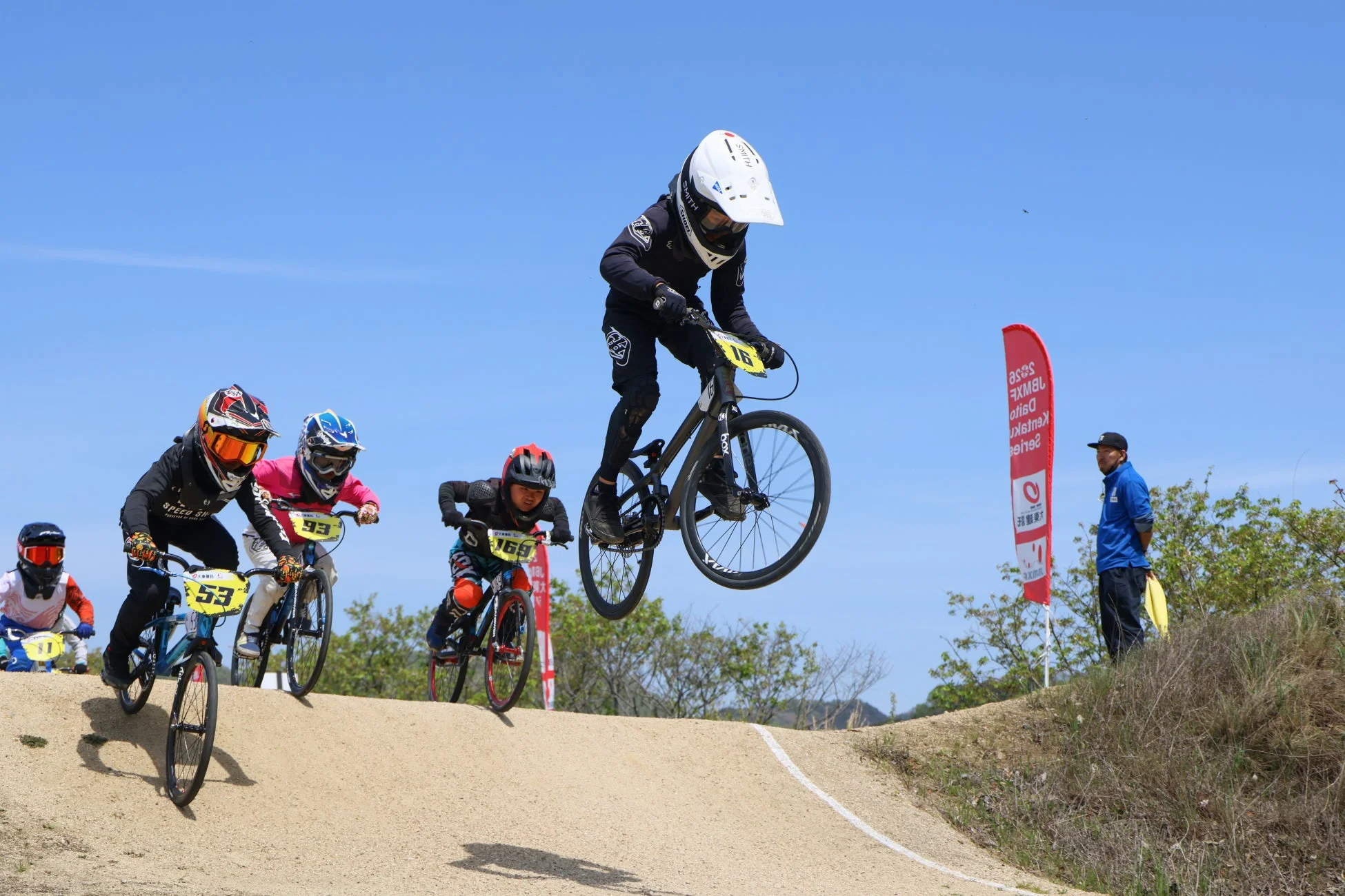青い空の下、ダートトラックでBMXレースをしている子供たちの写真