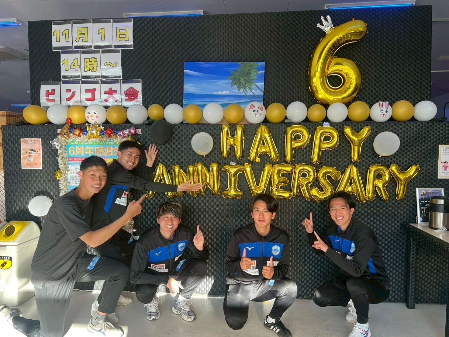 5人の若い男性が6周年記念の飾り付けの前でポーズをとっています