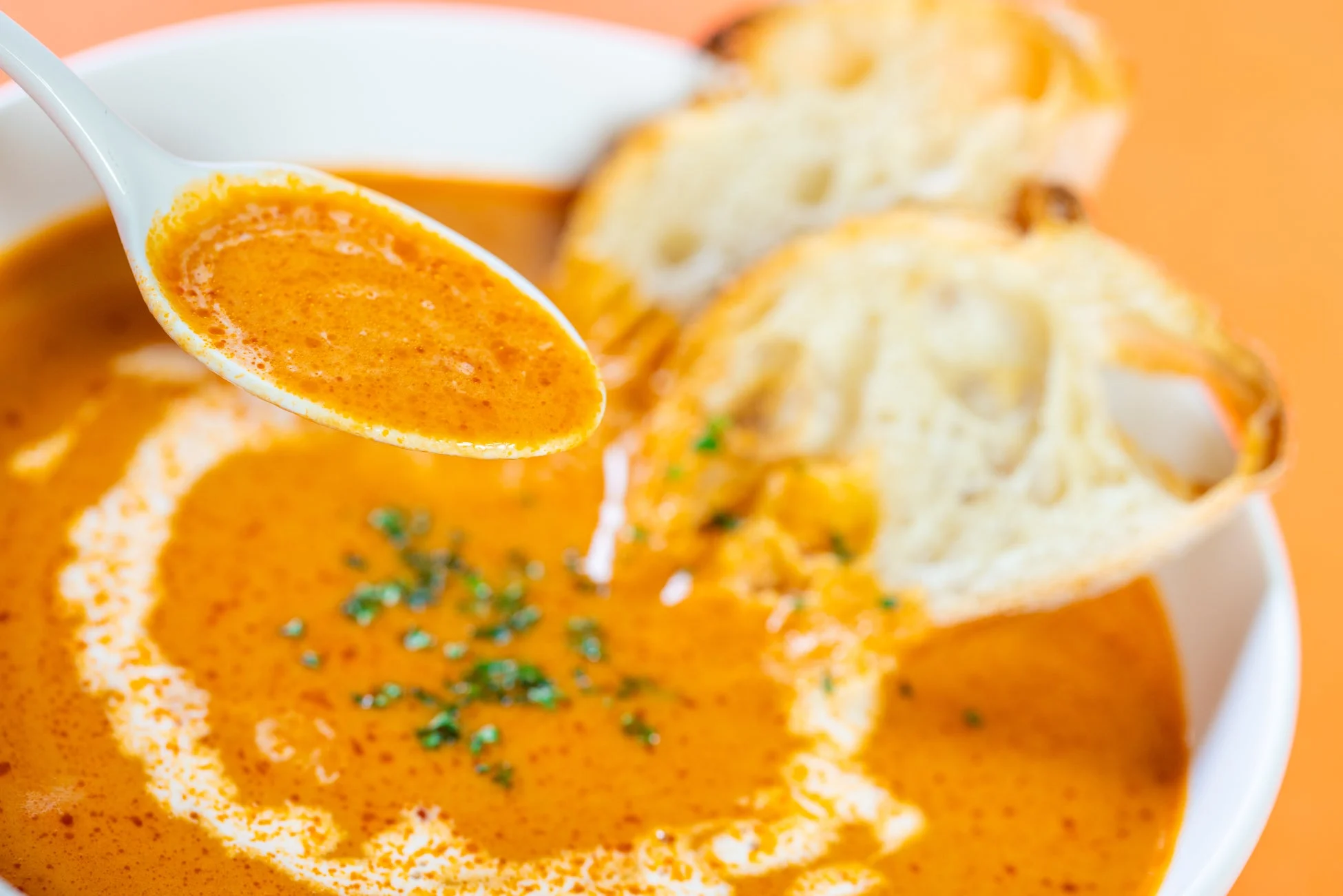 オレンジ色の温かいスープが白いボウルに入っており、スプーンで一口すくわれています