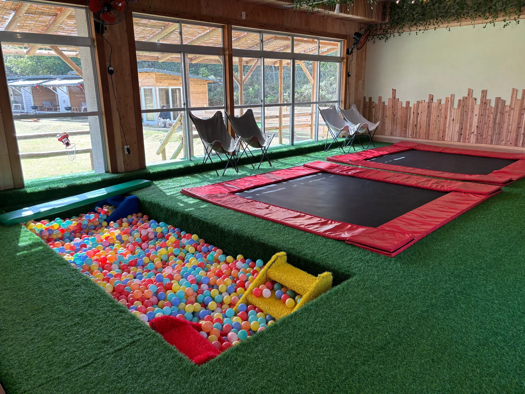人工芝が敷かれた広々とした室内遊び場で、カラフルなボールプールと2つのトランポリンが設置されている