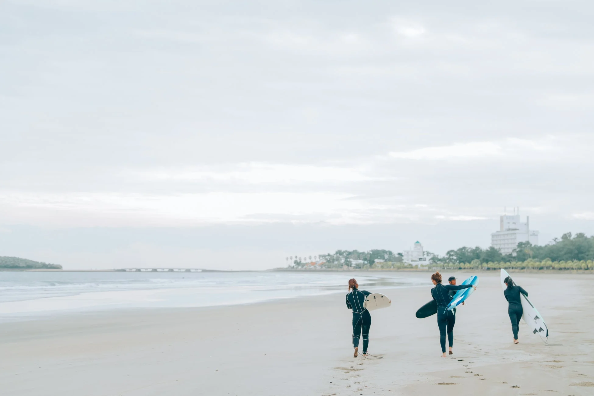 ウェットスーツを着た3人の人物が、サーフボードを抱えて広々とした砂浜を歩いています。