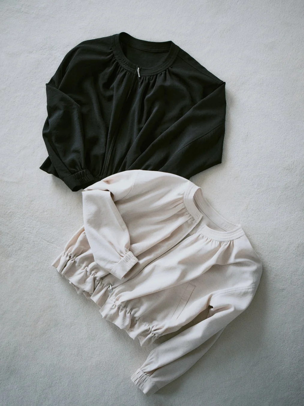 黒とベージュの2色のジップアップブルゾンが白い背景に平置きされています。袖口と裾にギャザーが入ったカジュアルなデザインで、春秋のアウターとして活躍しそうです。