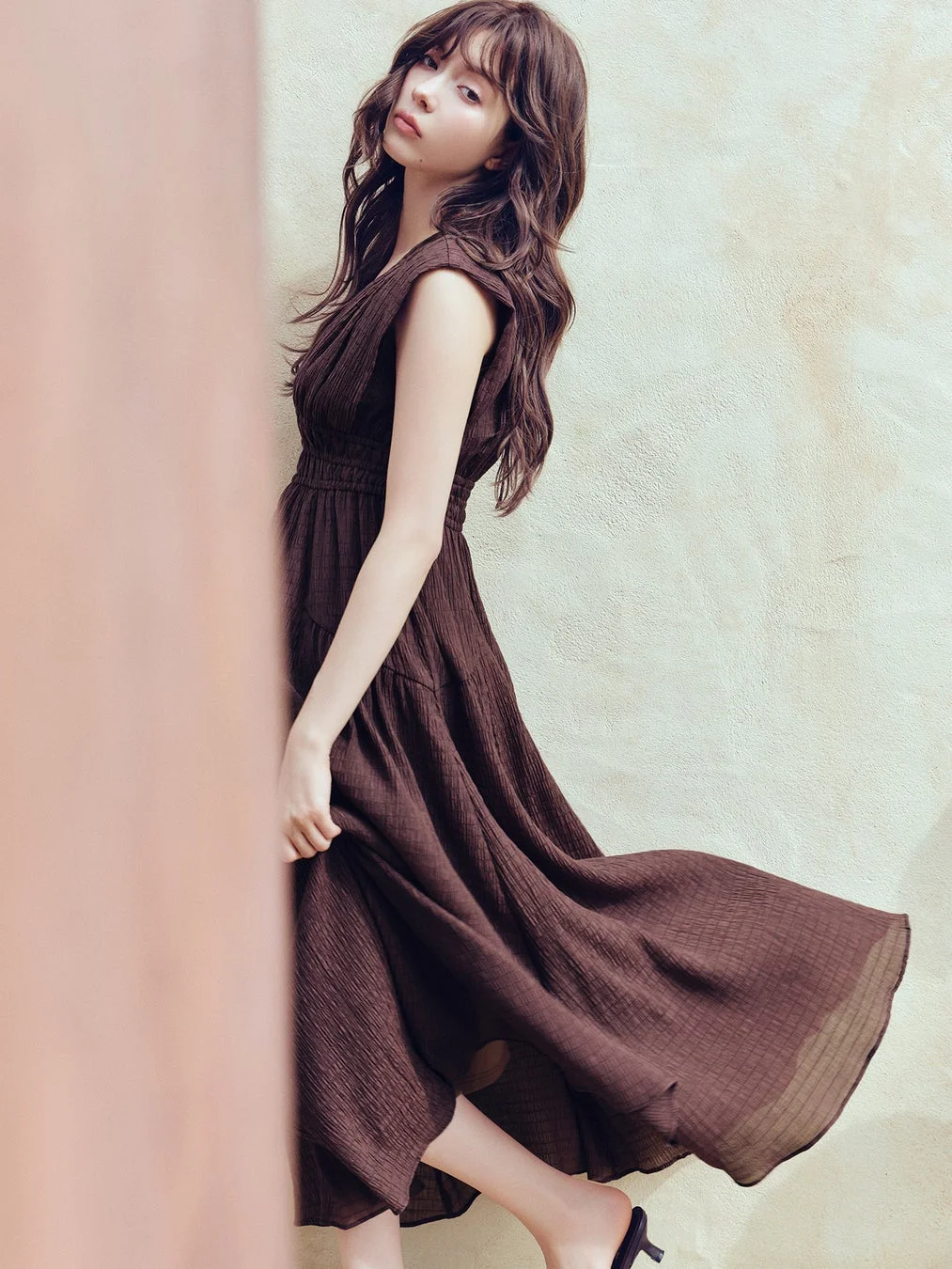 茶色のワンピースを着た女性が屋外でポーズをとっている画像です。