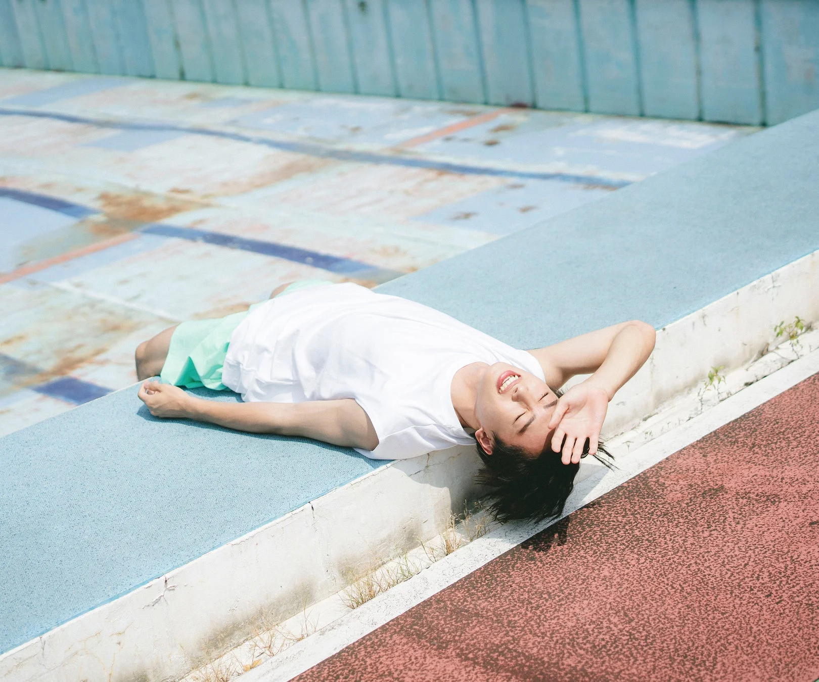 空のプールサイドで仰向けに横たわりリラックスする若い男性